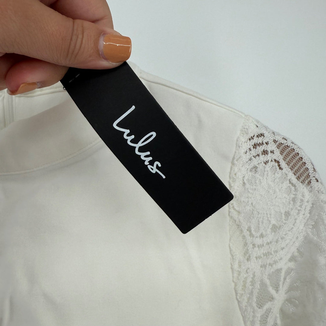Hand holding a Lulus tag against a white garment with lace details.