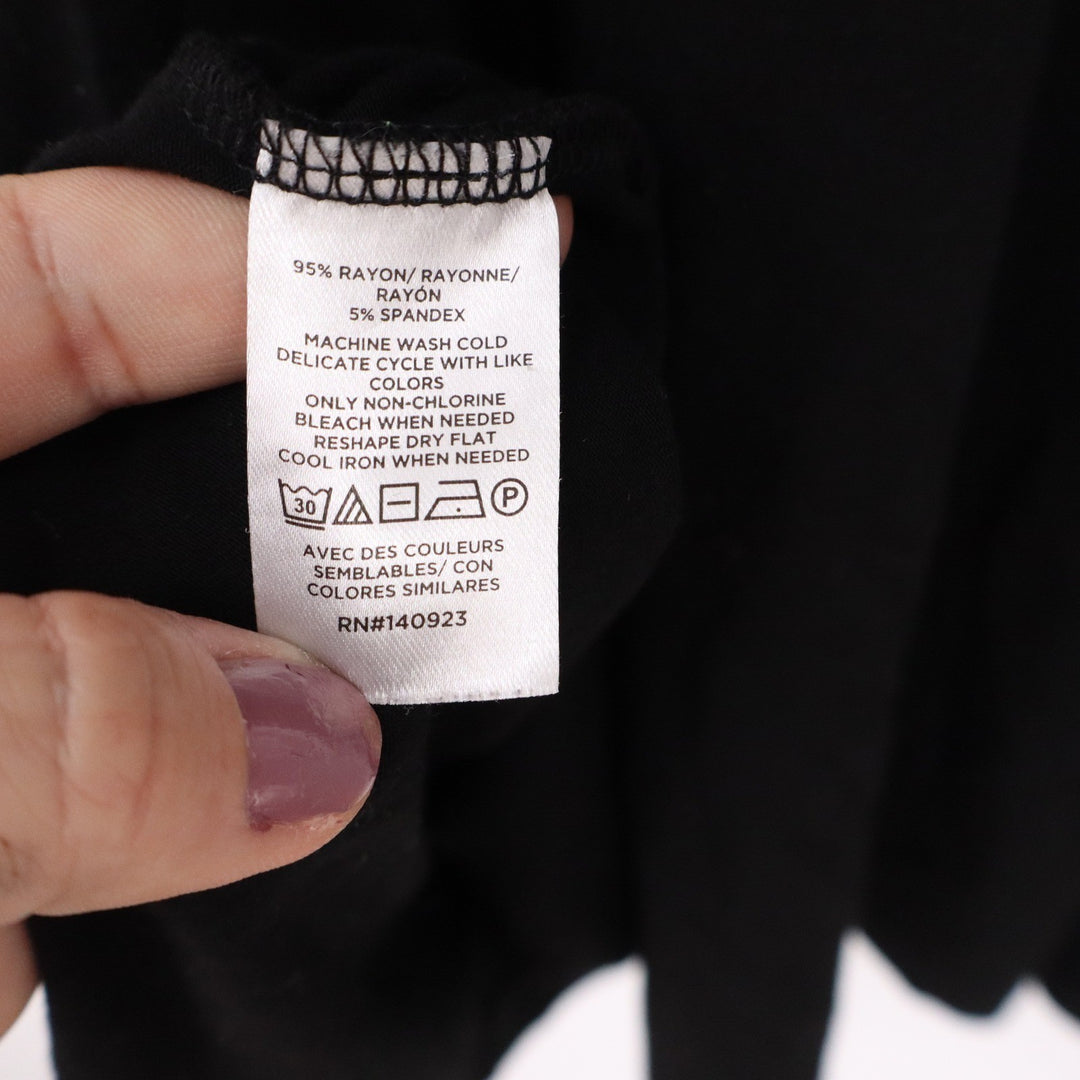 Clothing label with care instructions held by a hand against a dark fabric background