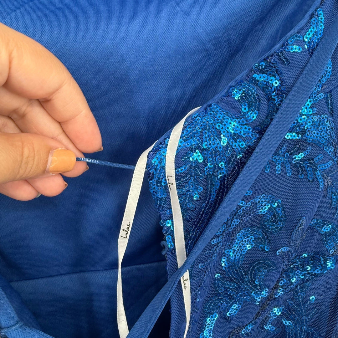 Close-up of a hand holding a blue fabric with intricate patterns and a label.