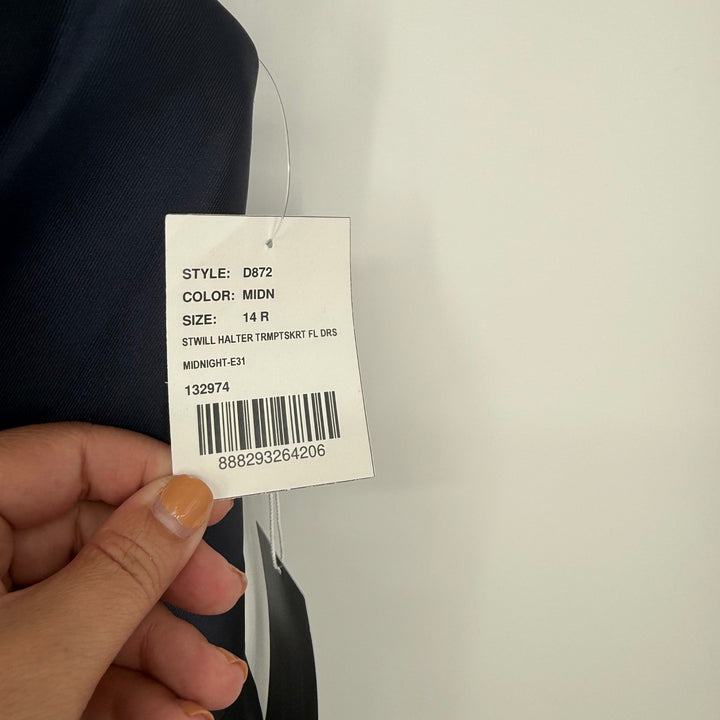 Hand holding a clothing tag with product details against a neutral background