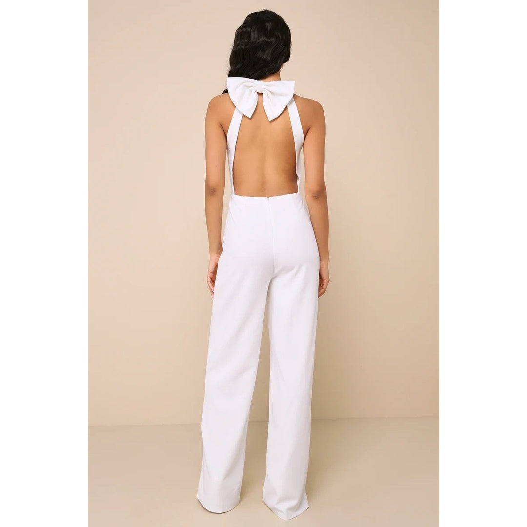 Woman wearing a white jumpsuit with a bow detail on the back against a beige background