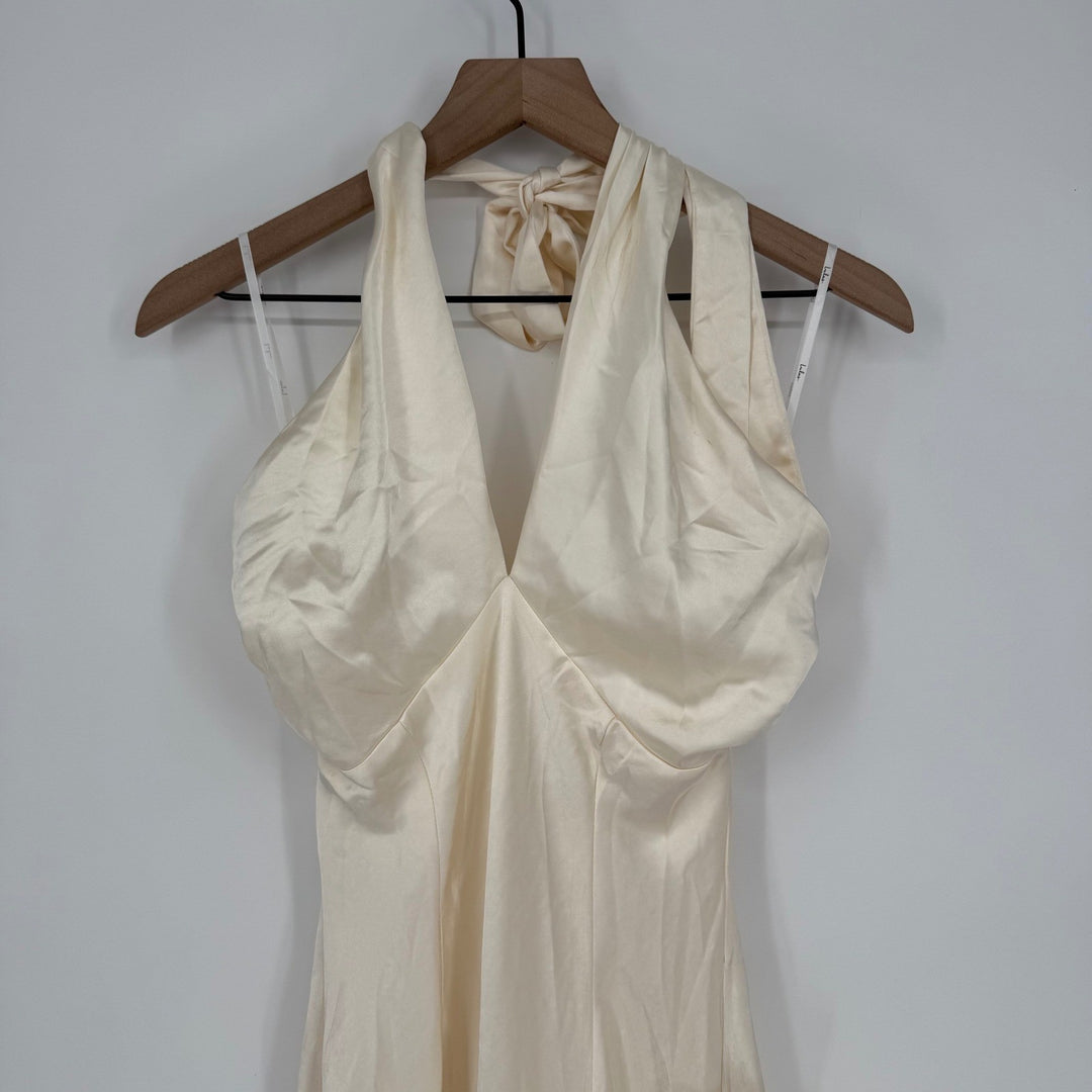 Beige halter neck dress on a wooden hanger against a white wall