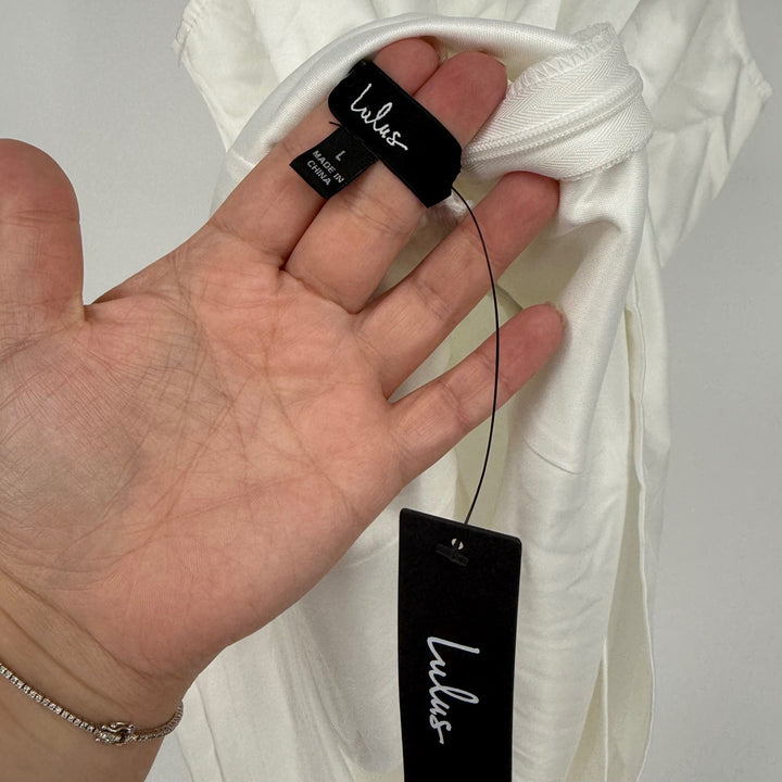Hand holding a Lulus tag against a white garment with a plain background