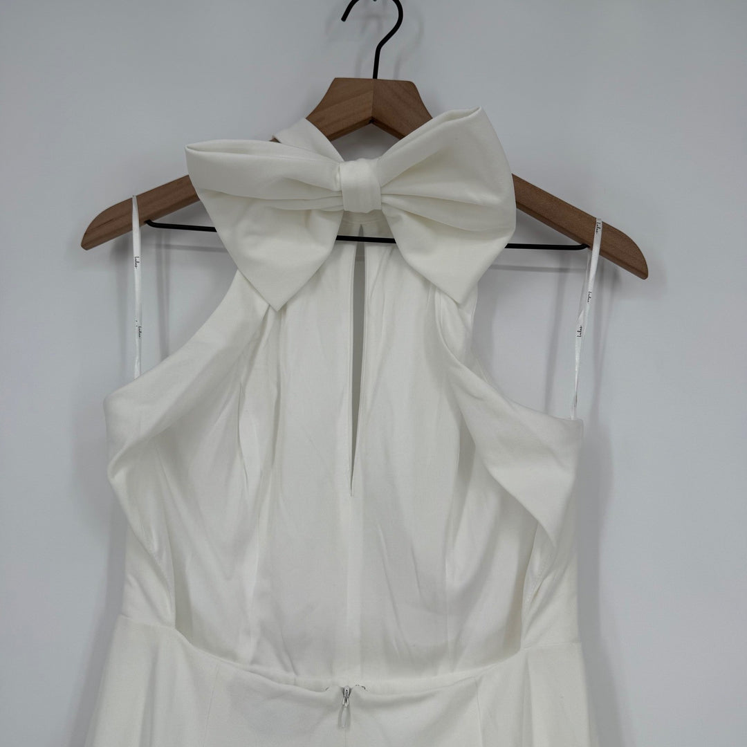White dress with a large bow on a wooden hanger against a white background