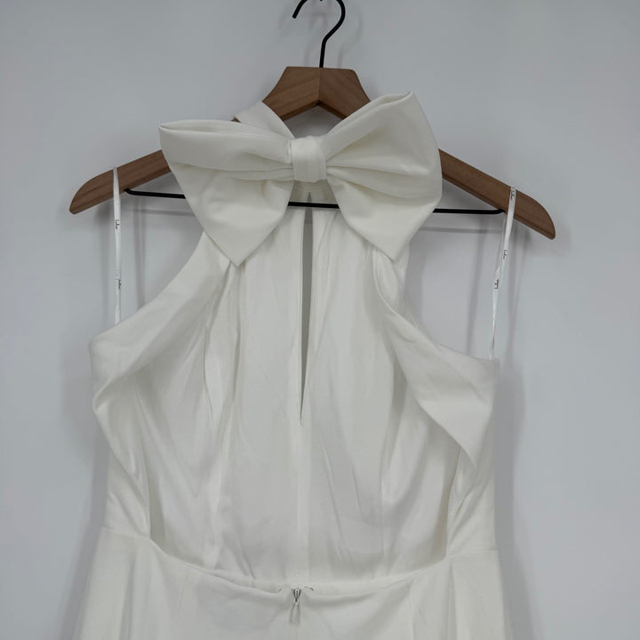 White dress with a large bow on a wooden hanger against a white background